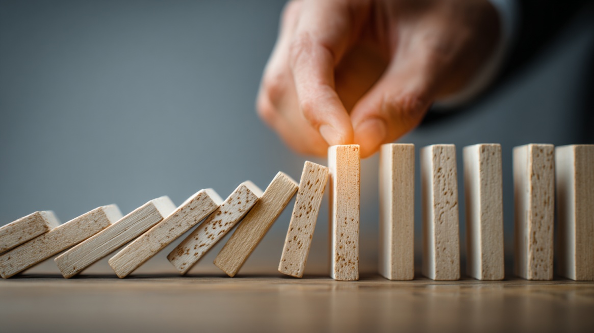 Hand stopping falling domino blocks to prevent a chain reaction